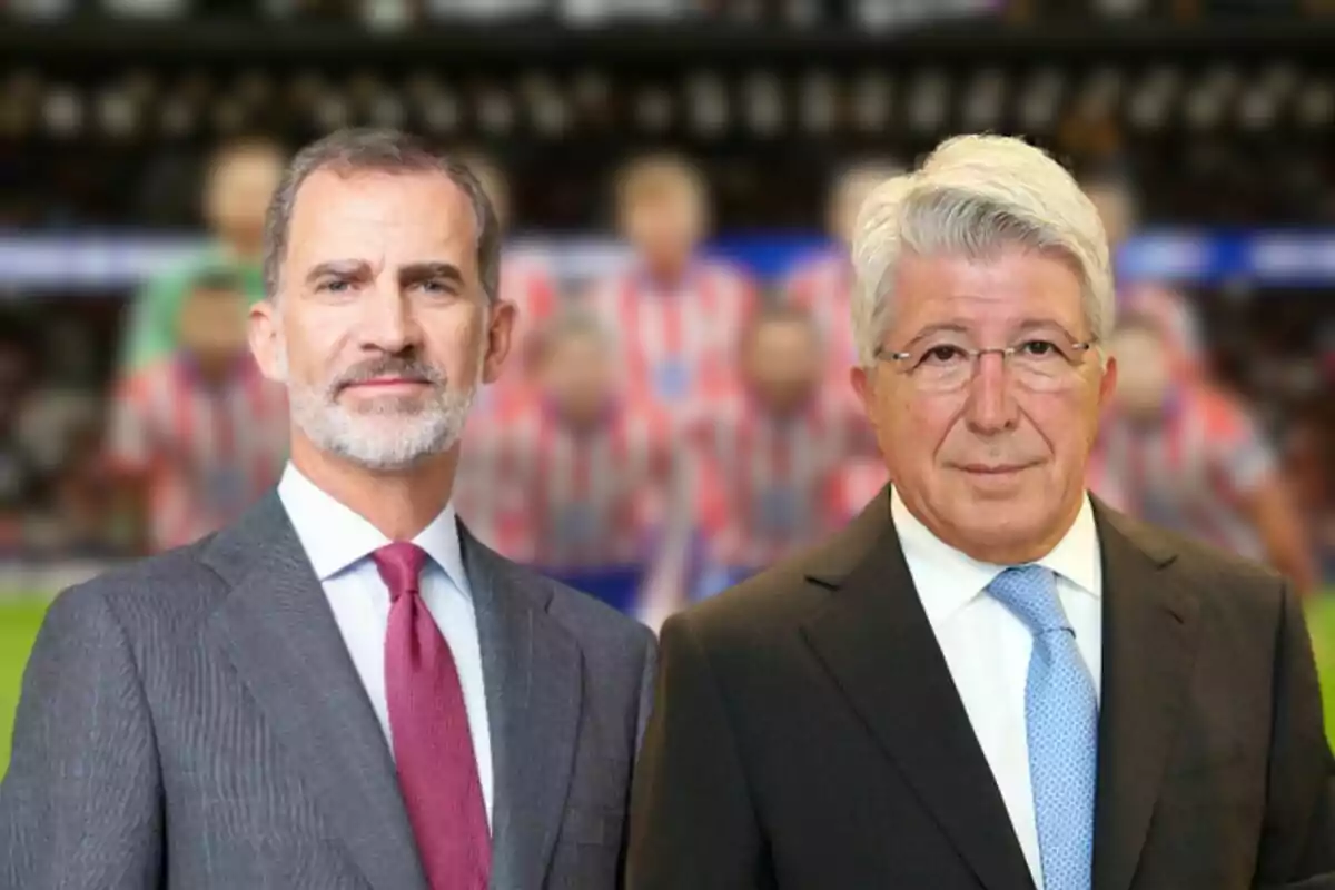 Dos hombres con traje posan frente a un fondo desenfocado de un estadio de fútbol.