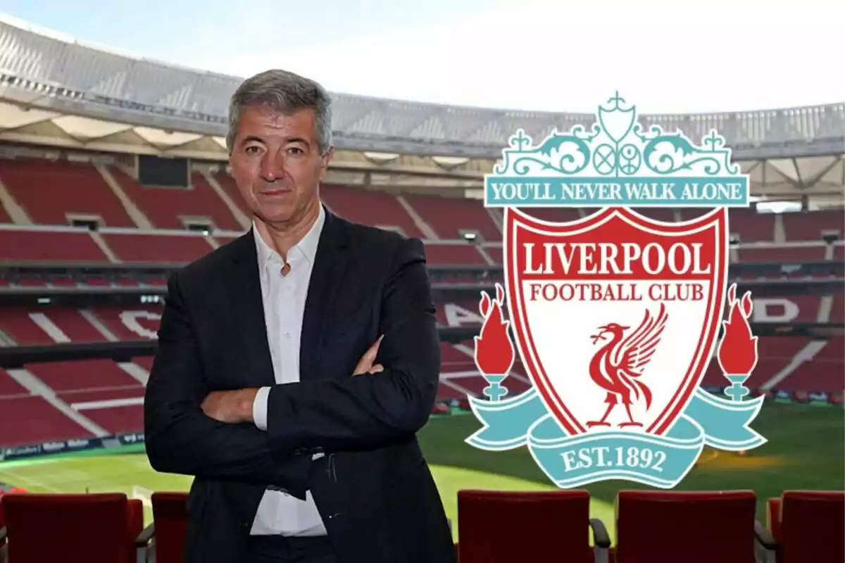 Un hombre de traje con los brazos cruzados en un estadio con el escudo del Liverpool Football Club al lado.