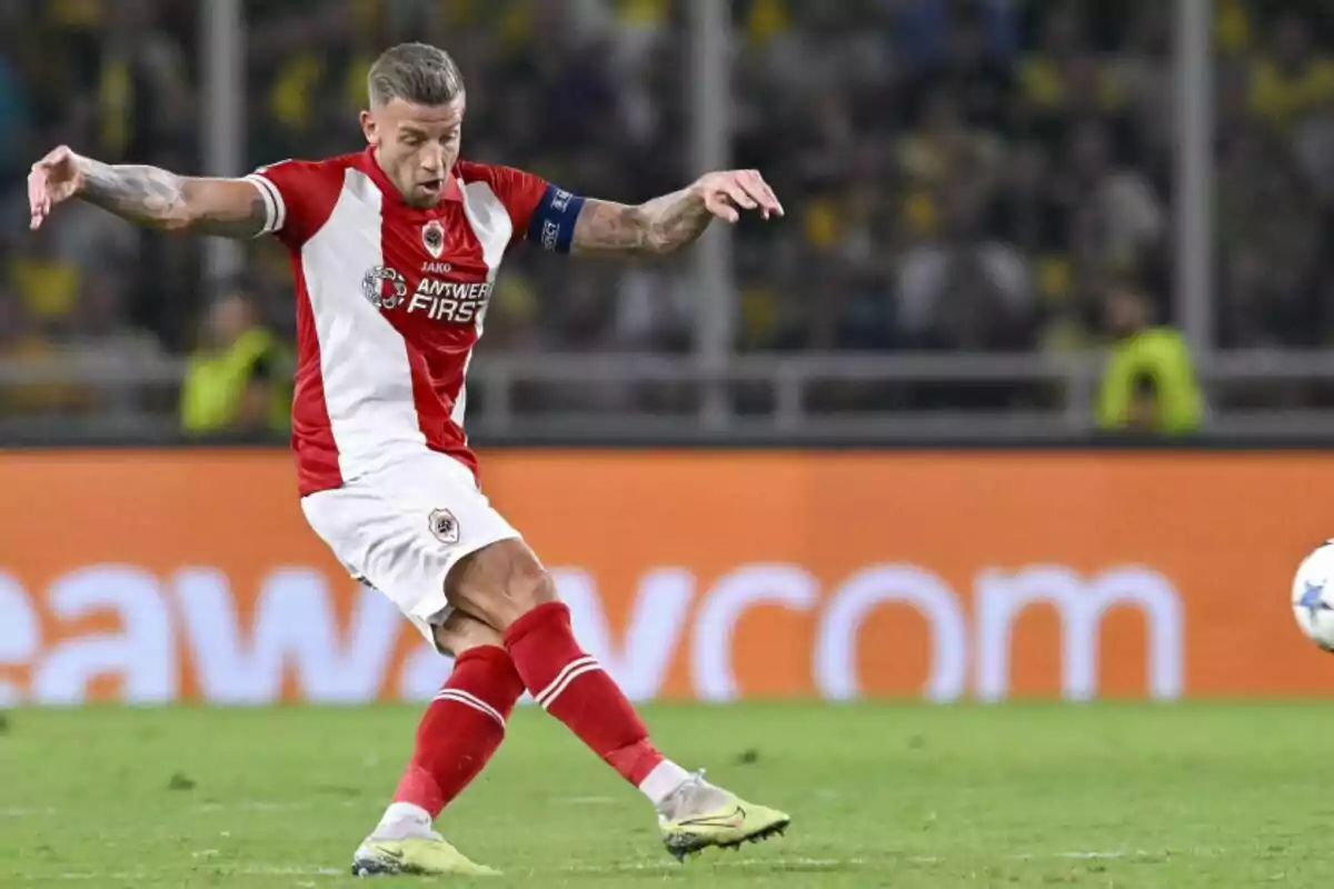 Jugador de fútbol con uniforme rojo y blanco pateando un balón en un estadio.