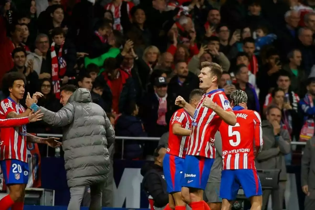 Jugadores de fútbol con uniforme rojo y blanco celebran en el campo mientras la multitud aplaude en el fondo.