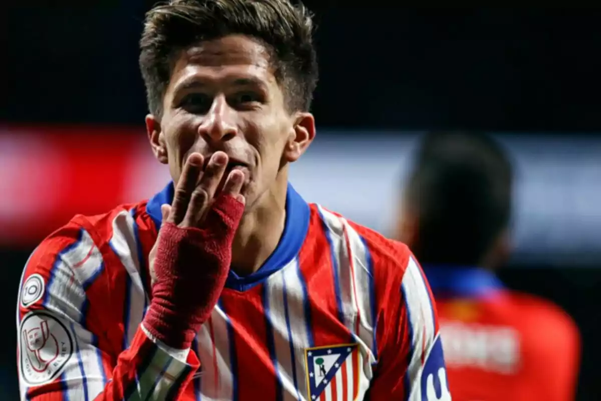 Un jugador de fútbol con uniforme rojo y blanco sopla un beso con la mano vendada.