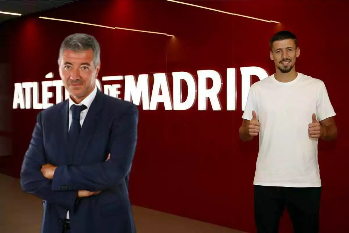 Dos hombres posan frente a un letrero iluminado que dice "Atlético de Madrid", uno de ellos está vestido con un traje azul y el otro con una camiseta blanca, haciendo un gesto de aprobación con ambos pulgares.