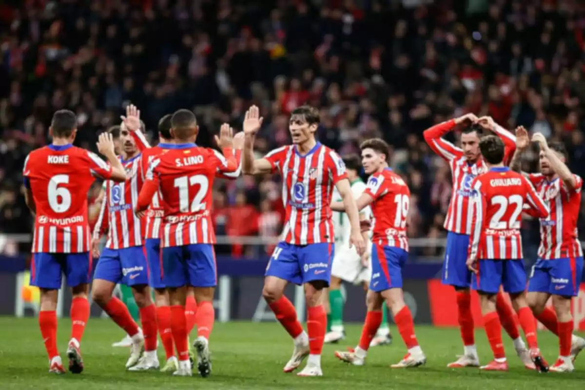 Jugadores de fútbol con uniforme rojo y blanco celebrando en el campo.