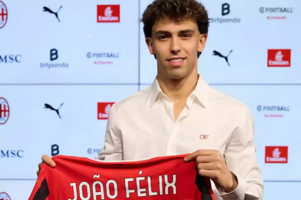 Un hombre sosteniendo una camiseta de fútbol roja con su nombre en un evento de presentación.