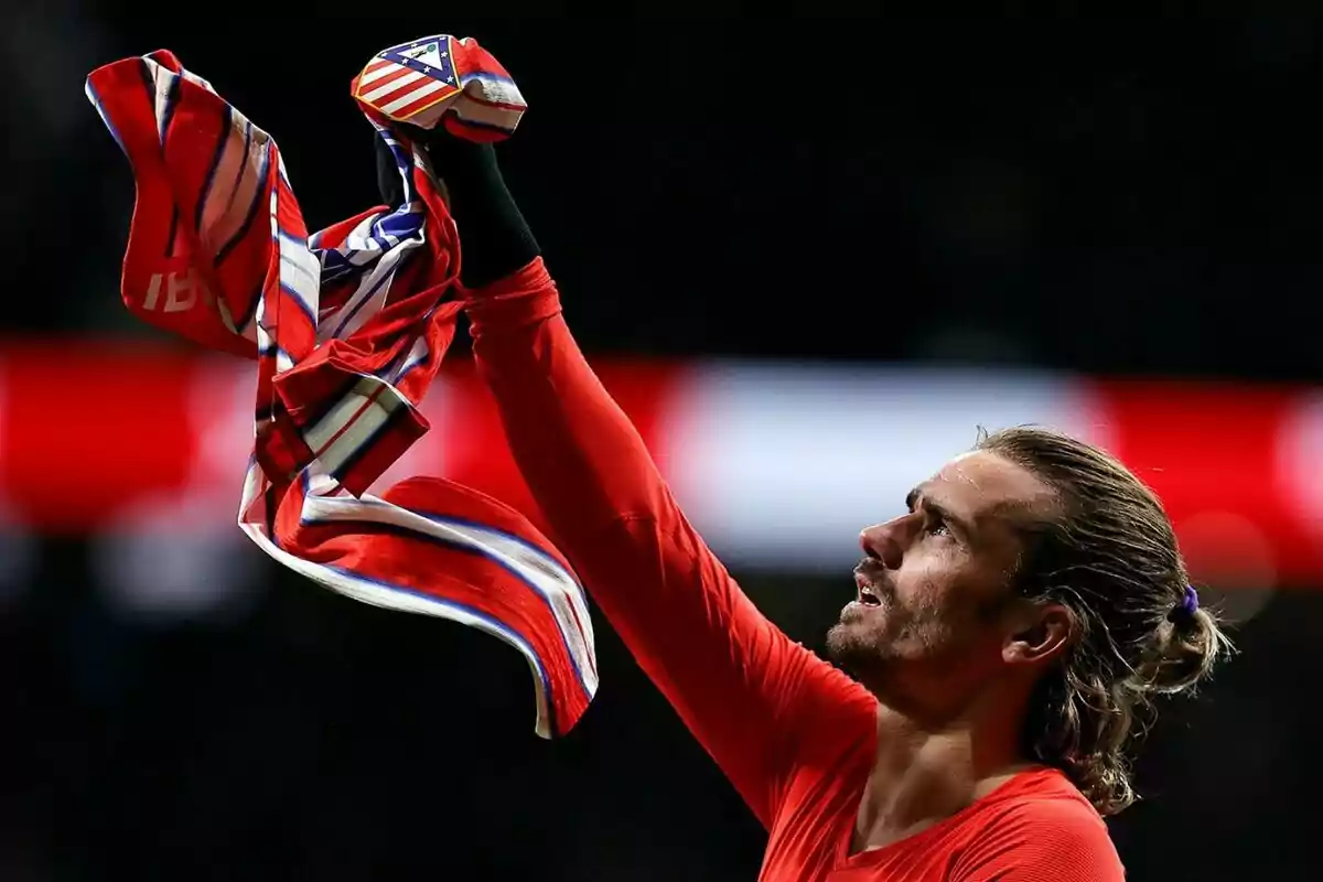 Persona levantando una camiseta del Atlético de Madrid en un estadio.