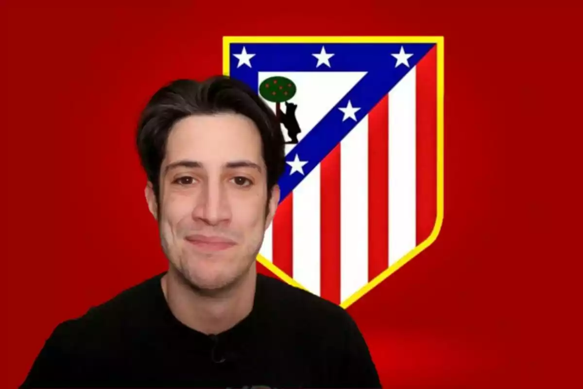 Un hombre sonriente frente al escudo del Atlético de Madrid sobre un fondo rojo.