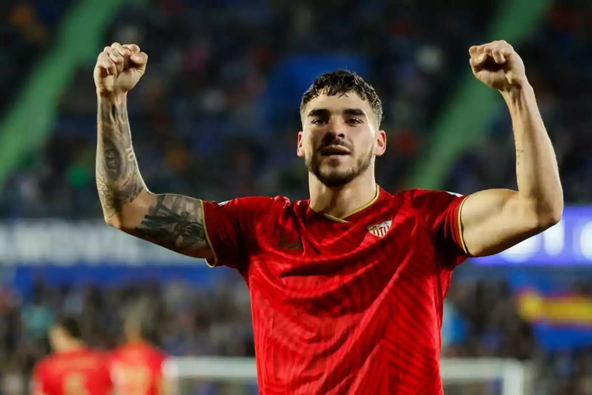 Jugador de fútbol con camiseta roja levantando los brazos en señal de victoria. Jugador de fútbol con camiseta roja levantando los brazos en señal de victoria.