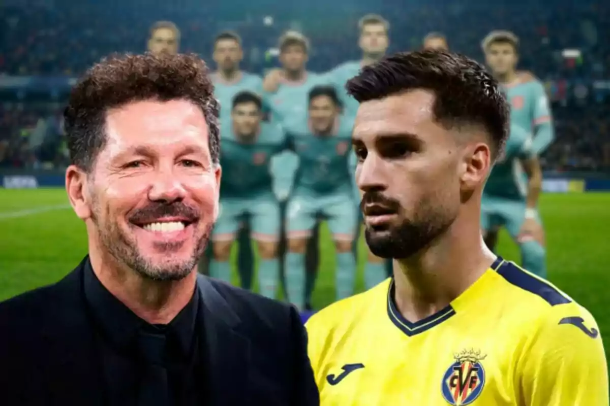 Dos hombres en primer plano, uno con traje negro y otro con camiseta amarilla de fútbol, con un equipo de jugadores desenfocados al fondo en un estadio.