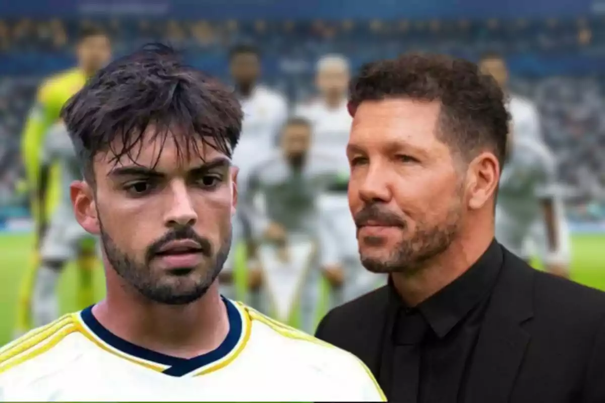 Dos hombres en un campo de fútbol con jugadores desenfocados al fondo.