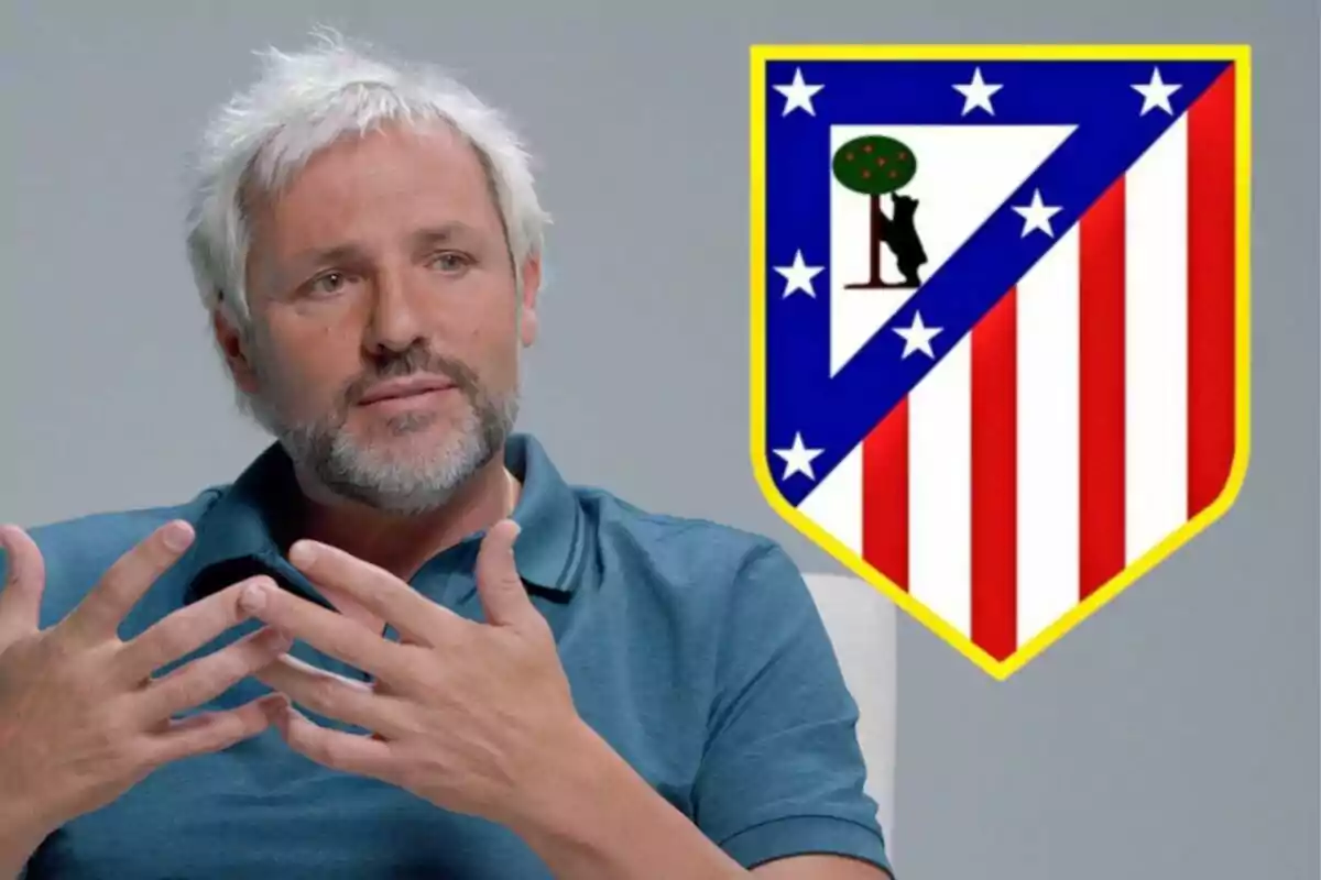 Un hombre de cabello canoso y barba está sentado con las manos levantadas, junto al escudo del Atlético de Madrid.