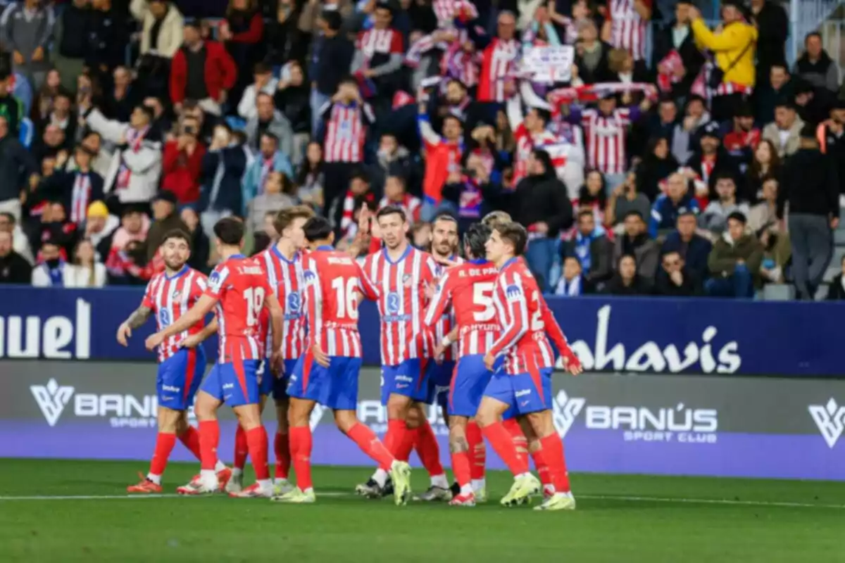 Jugadores de fútbol con uniforme a rayas rojas y blancas celebran en el campo mientras la multitud los anima desde las gradas.