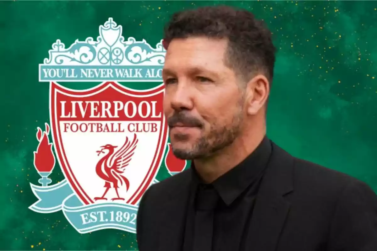 A man in a dark suit in front of the Liverpool Football Club crest on a green background.