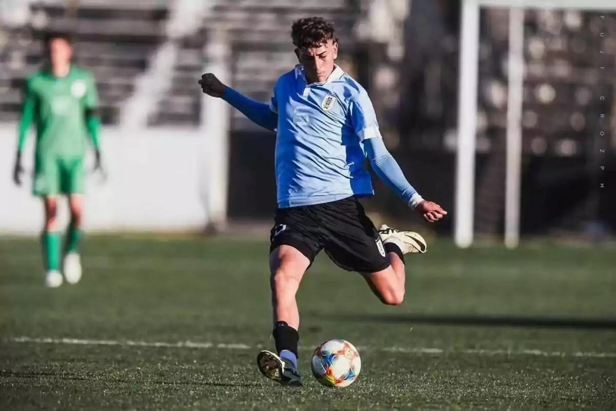 Jugador de fútbol con uniforme celeste pateando un balón en el campo de juego.