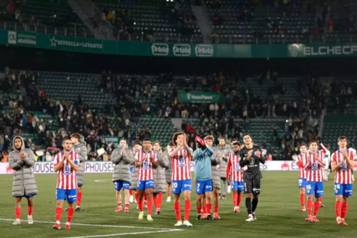 Jugadores de fútbol con uniforme de rayas rojas y blancas aplauden en un estadio después de un partido.