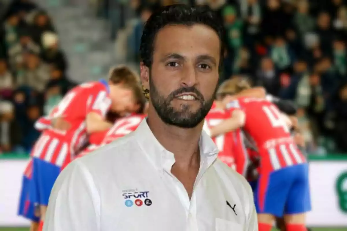 Un hombre con barba y camisa blanca está de pie frente a un grupo de jugadores de fútbol que llevan uniformes a rayas rojas y blancas.