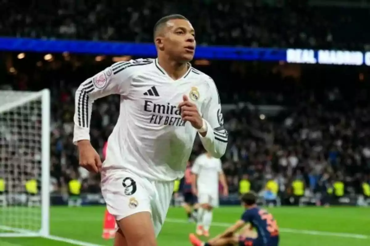 Un jugador de fútbol con uniforme blanco corre en un estadio lleno de espectadores.