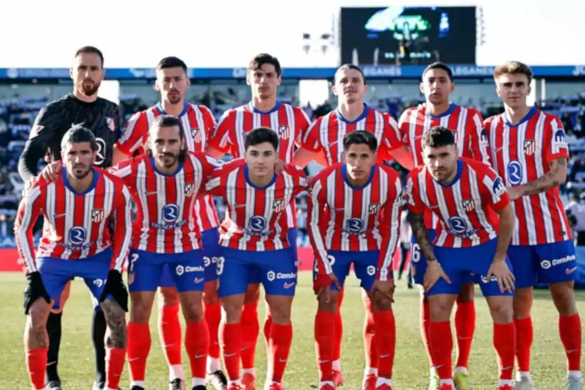 Un equipo de fútbol posando en el campo con uniformes a rayas rojas y blancas.