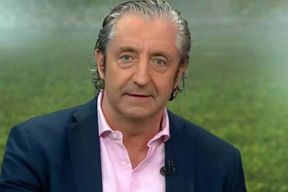 Un hombre de cabello canoso y ojos claros, vistiendo una camisa rosa y un saco oscuro, aparece en un entorno de estudio de televisión.