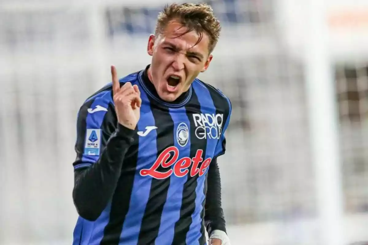 Un jugador de fútbol con uniforme azul y negro celebra con entusiasmo levantando un dedo.