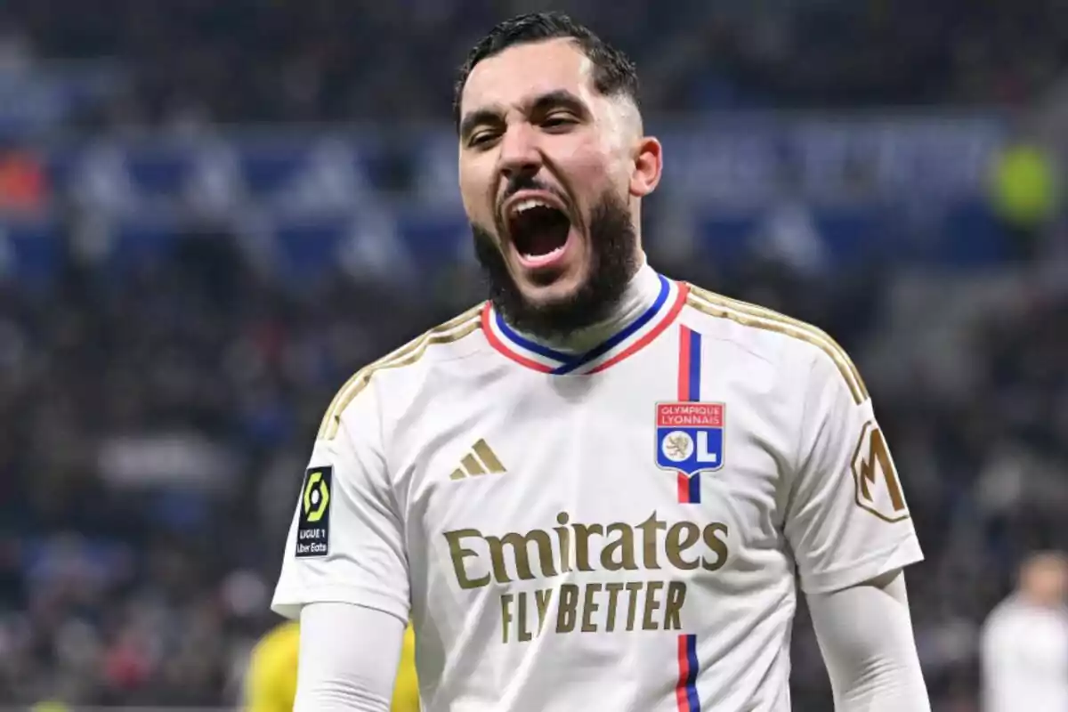 Un jugador de fútbol con uniforme blanco del Olympique de Lyon grita con emoción en el campo.