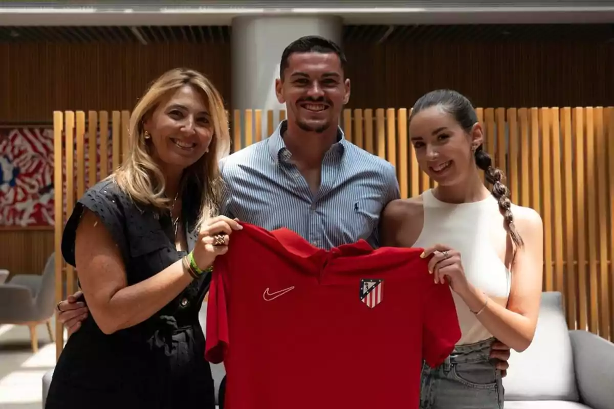 Tres personas sonrientes sosteniendo una camiseta roja del Atlético de Madrid.