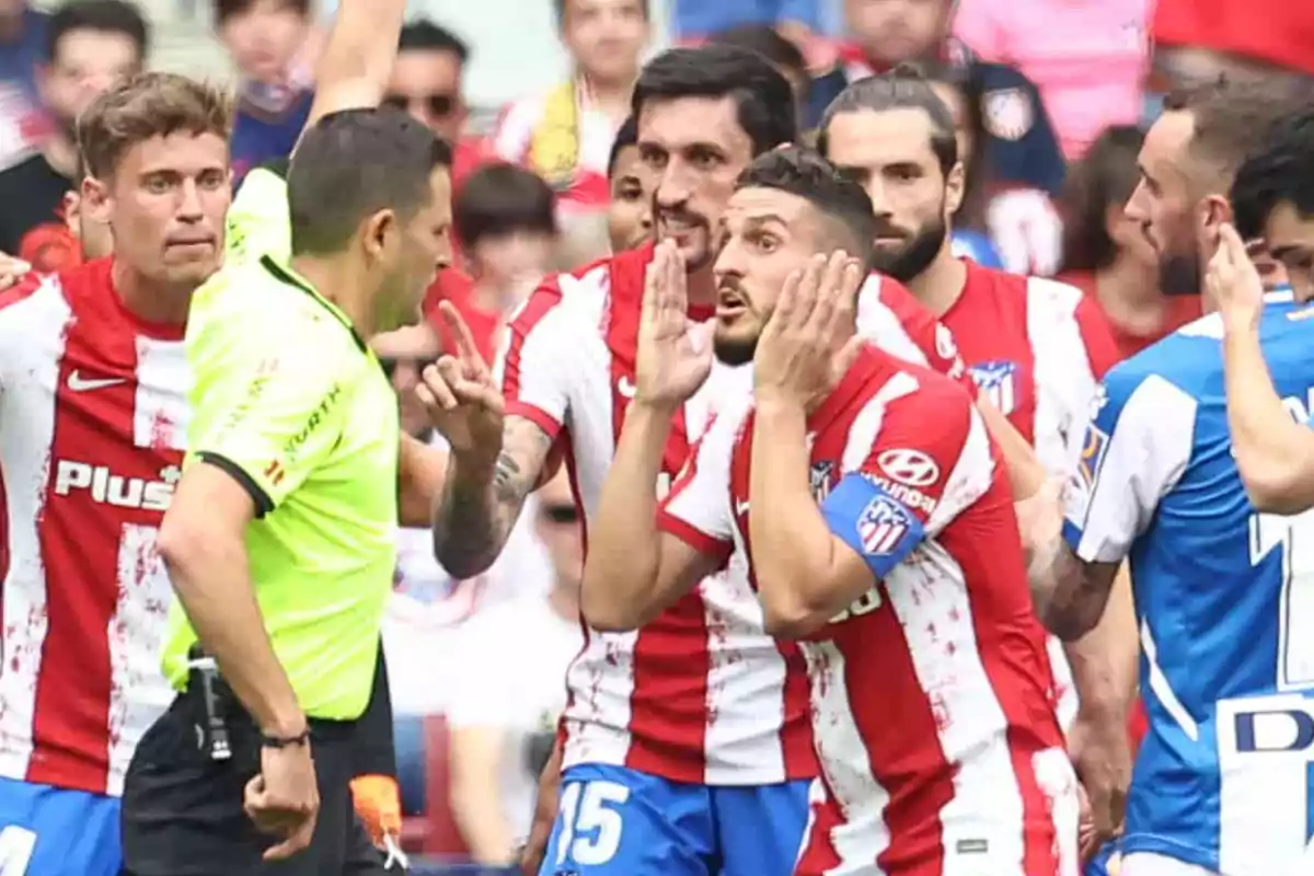 Jugadores de fútbol del Atlético de Madrid discuten con el árbitro durante un partido.