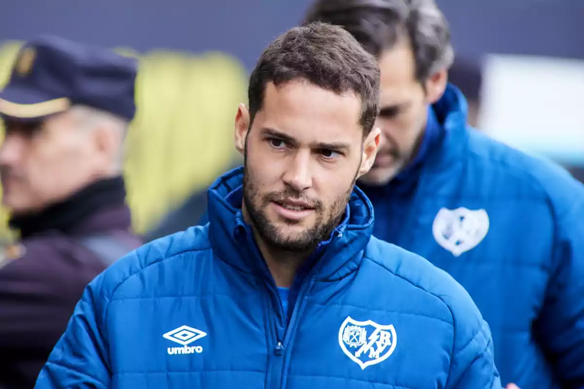 Hombre con chaqueta azul del Rayo Vallecano y logotipo de Umbro en un entorno deportivo Hombre con chaqueta azul del Rayo Vallecano y logotipo de Umbro en un entorno deportivo