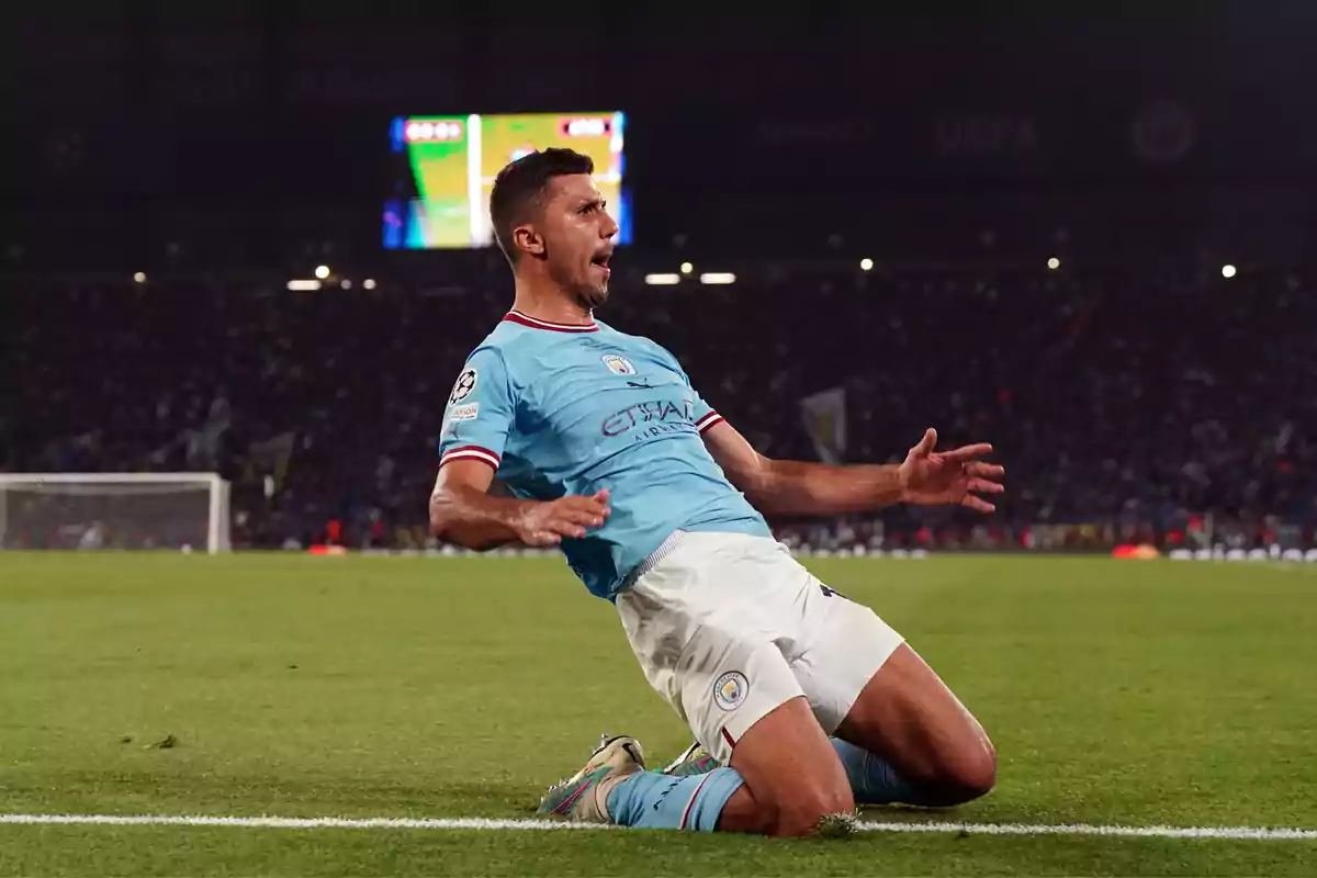 Un jugador de fútbol celebra deslizándose de rodillas sobre el césped durante un partido nocturno.