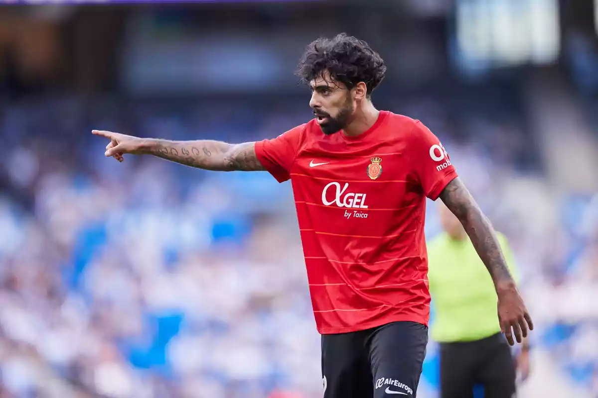 Jugador de fútbol con camiseta roja señalando con el brazo extendido en un estadio.