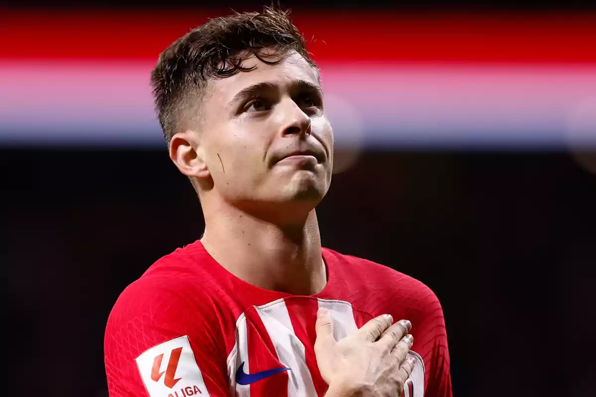 Jugador de fútbol con uniforme rojo y blanco, con la mano en el pecho, en un estadio.