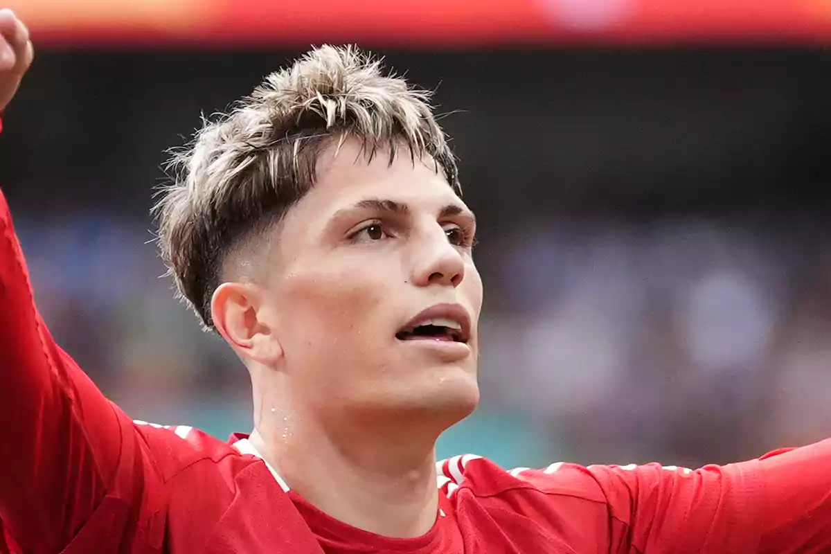 Un jugador de fútbol con camiseta roja celebra en el campo.