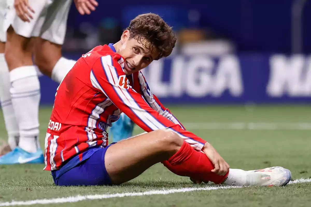 Jugador de fútbol sentado en el campo con expresión de dolor.