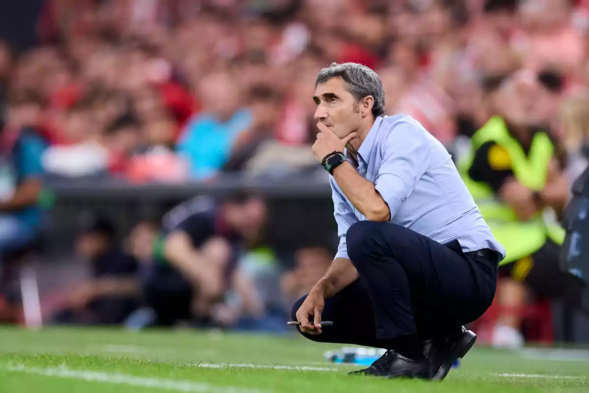 Un entrenador de fútbol agachado en la línea de banda durante un partido, observando atentamente el juego.