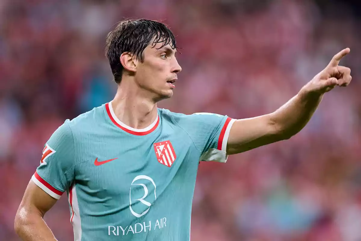 Jugador de fútbol con camiseta verde claro del Atlético de Madrid señalando con el dedo en un estadio.