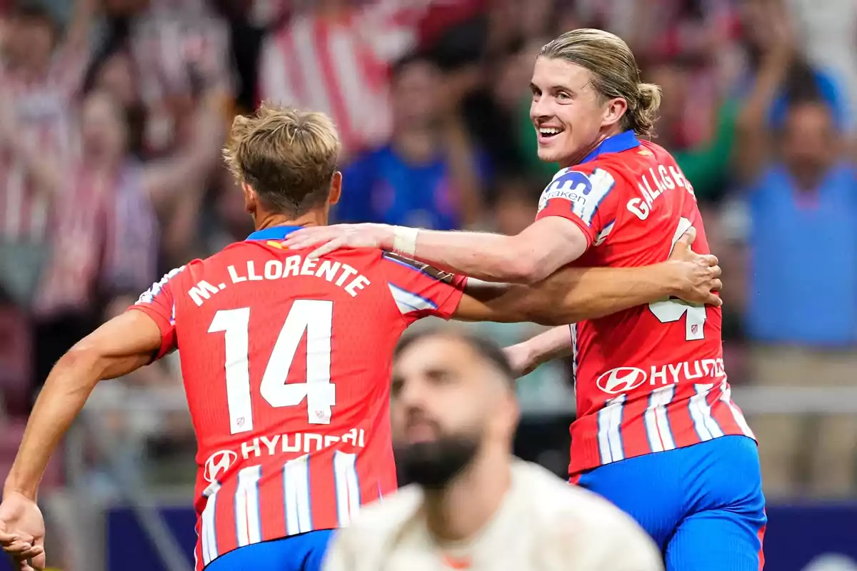 Dos jugadores de fútbol celebrando un gol con camisetas rojas y blancas.