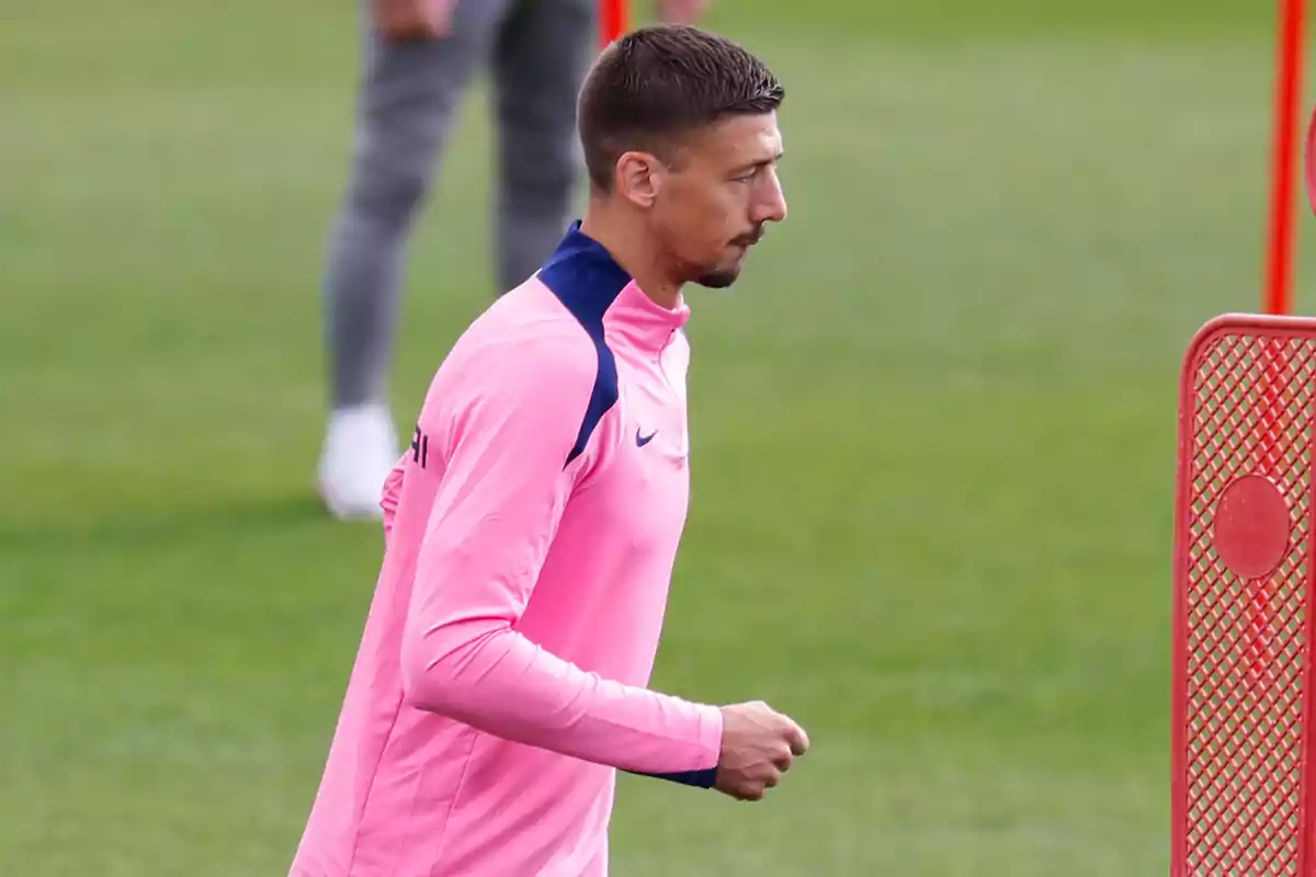 Un jugador de fútbol con una sudadera rosa entrenando en un campo de fútbol.