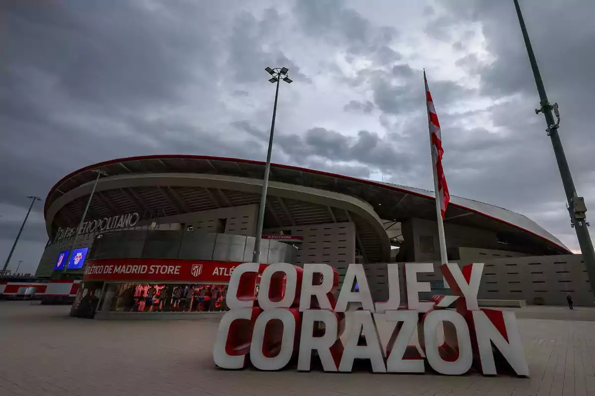 Vista del estadio Wanda Metropolitano con un letrero que dice "Coraje y Corazón" en primer plano y una tienda del Atlético de Madrid en el fondo.