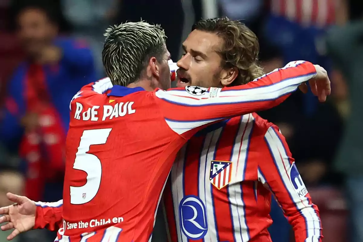 Dos jugadores de fútbol del Atlético de Madrid celebran un gol abrazándose en el campo.