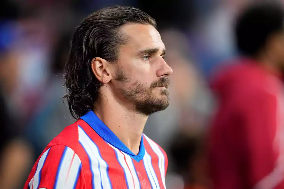 Un jugador de fútbol con una camiseta a rayas rojas, blancas y azules, mirando hacia la derecha.