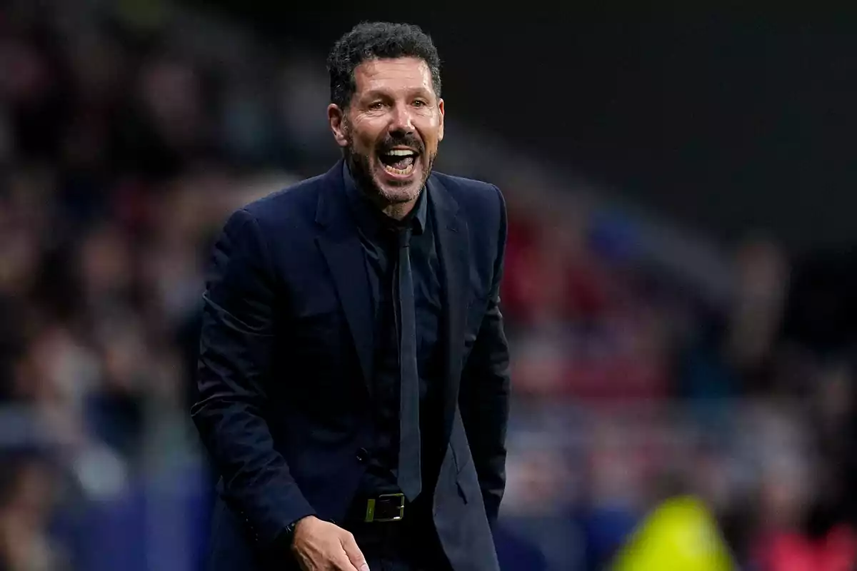 Hombre con traje oscuro gritando en un estadio de fútbol.