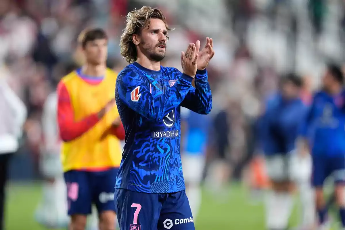 Jugador de fútbol aplaudiendo en el campo con uniforme azul y número 7.