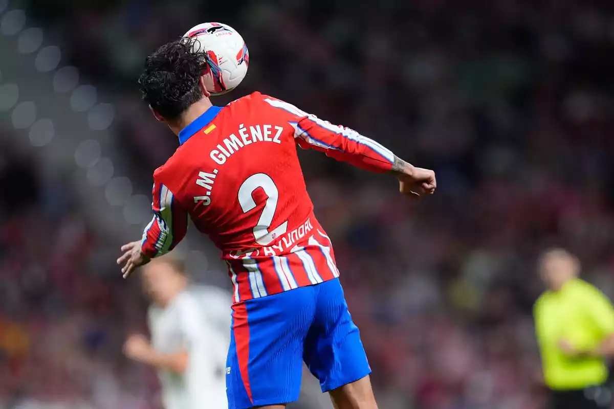 Un jugador de fútbol con el uniforme rojo y azul del Atlético de Madrid cabecea el balón durante un partido.