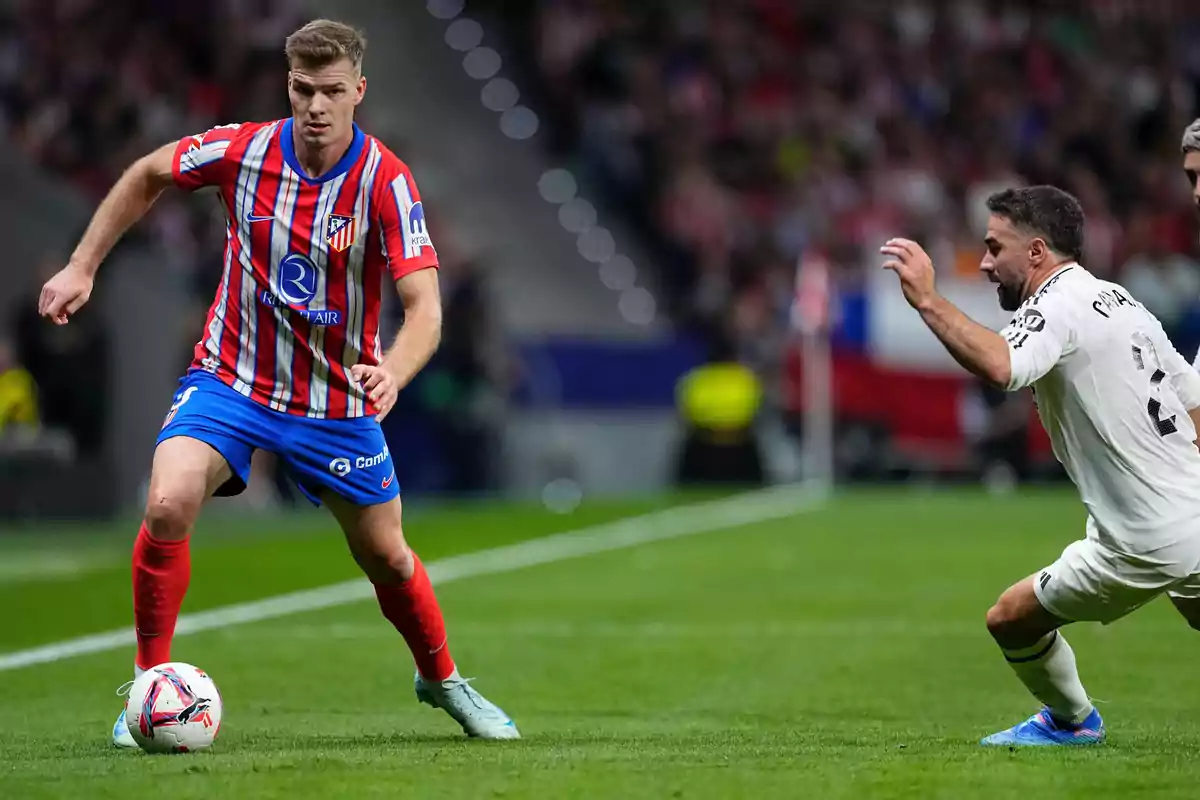 Un jugador del Atlético de Madrid controla el balón mientras un jugador del equipo contrario se aproxima para intentar quitarle la pelota durante un partido de fútbol.