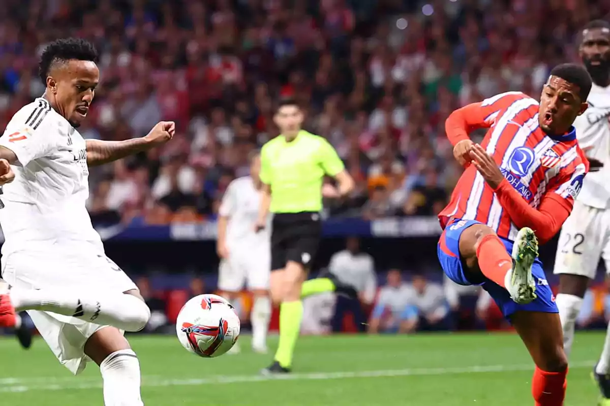 Dos jugadores de fútbol compiten por el balón durante un partido, uno con uniforme blanco y el otro con uniforme rojo y blanco, mientras un árbitro observa en el fondo.