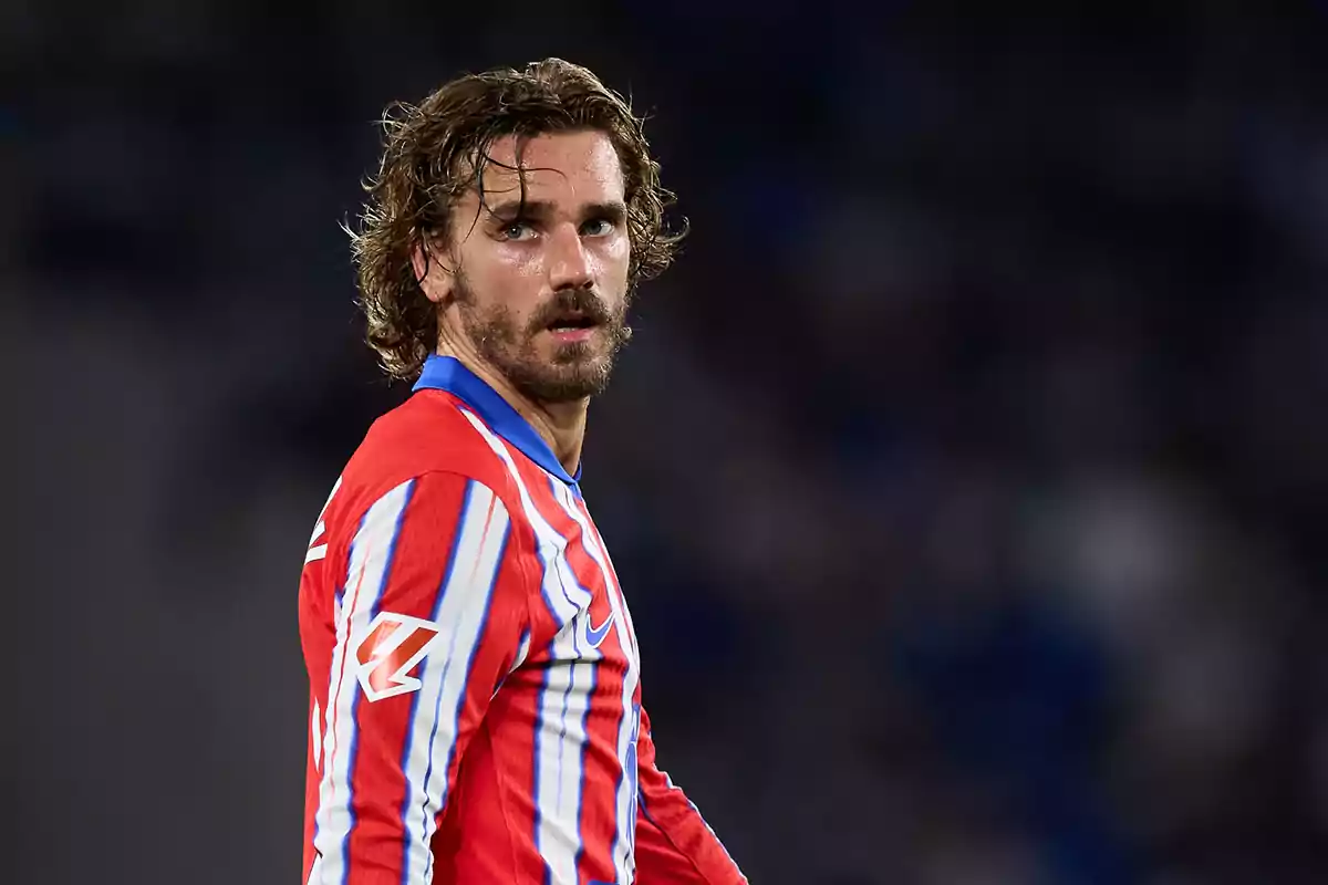 Un jugador de fútbol con uniforme rojo y azul mira hacia atrás en un campo de juego.