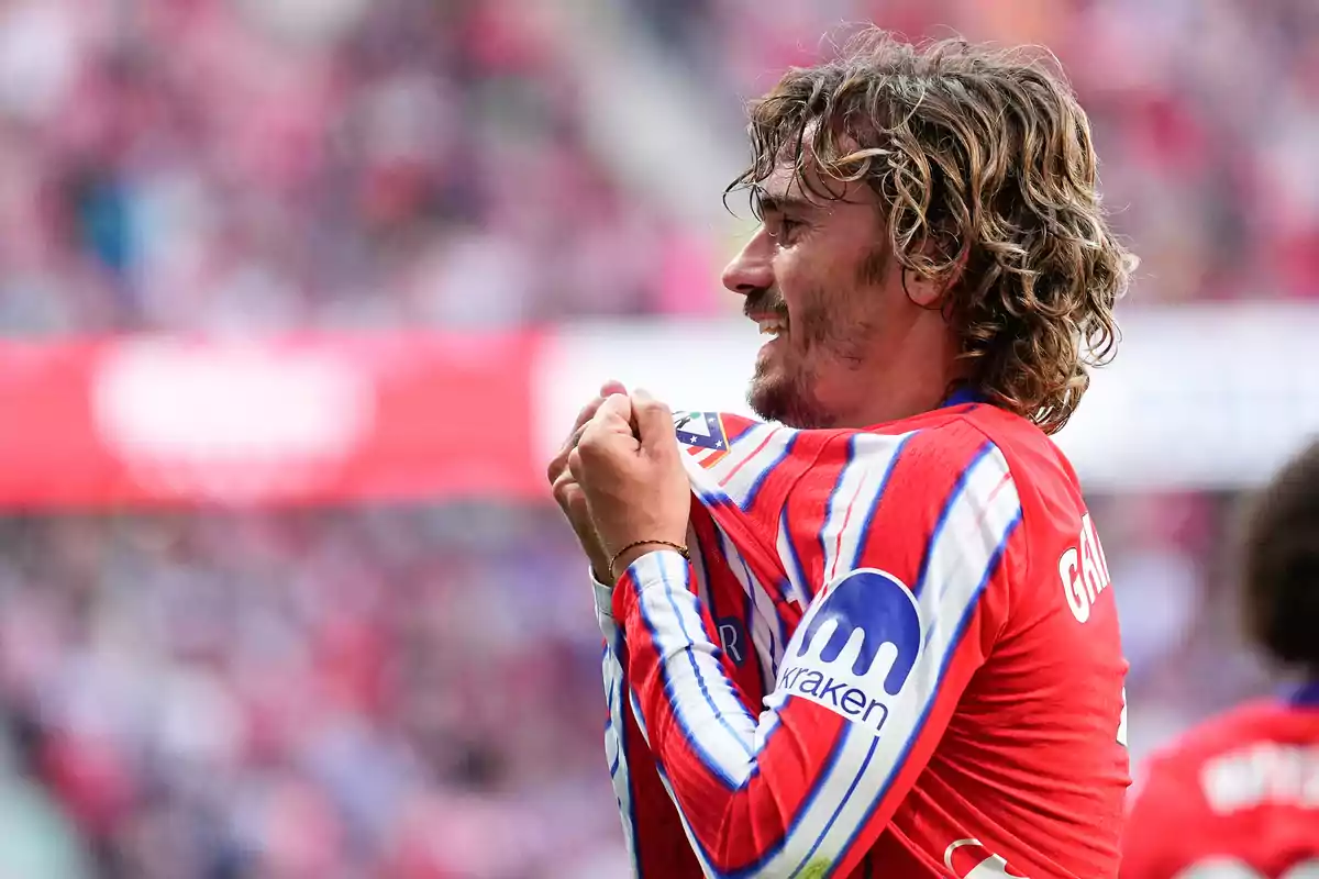 A soccer player in a red and blue uniform celebrates on the field.