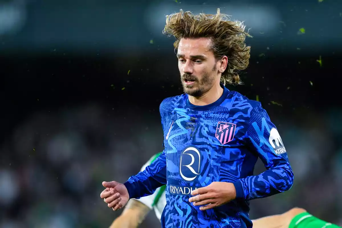 Un jugador de fútbol con uniforme azul y detalles en rosa corre en el campo durante un partido.