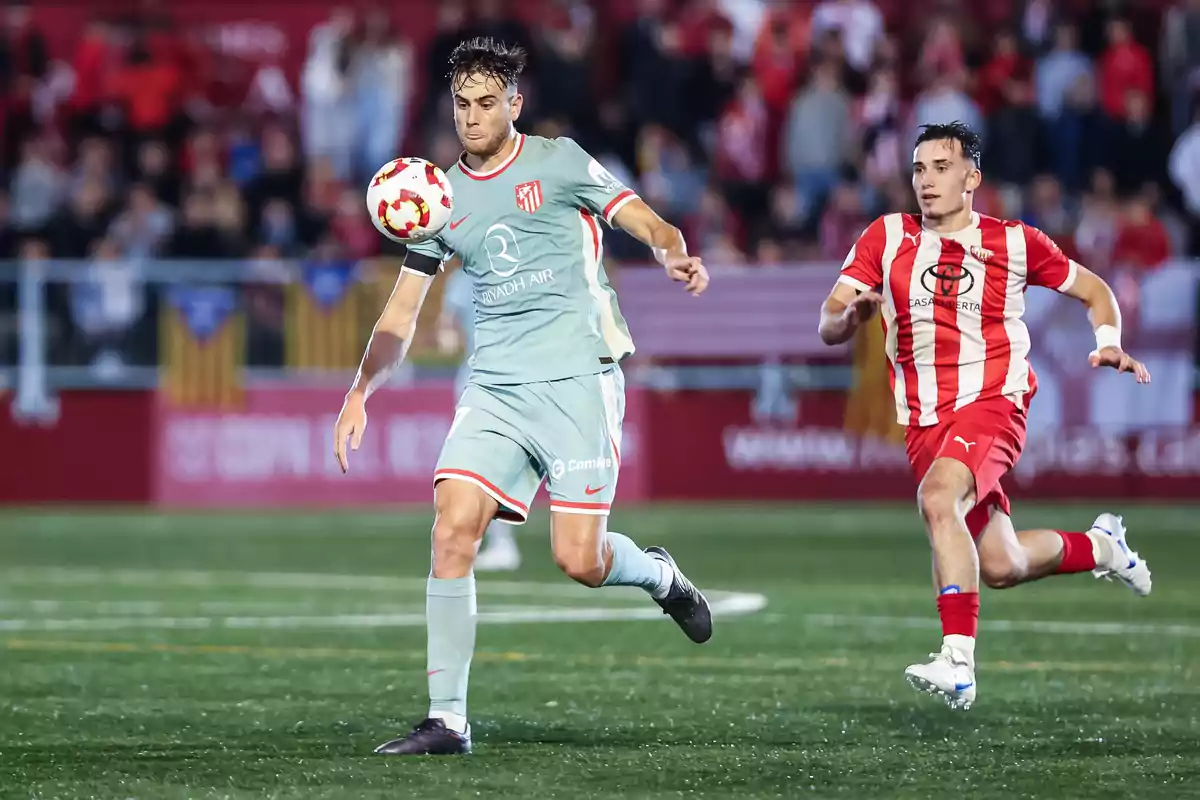 Dos futbolistas disputan el balón durante un partido en un estadio lleno de espectadores. Dos futbolistas disputan el balón durante un partido en un estadio lleno de espectadores.