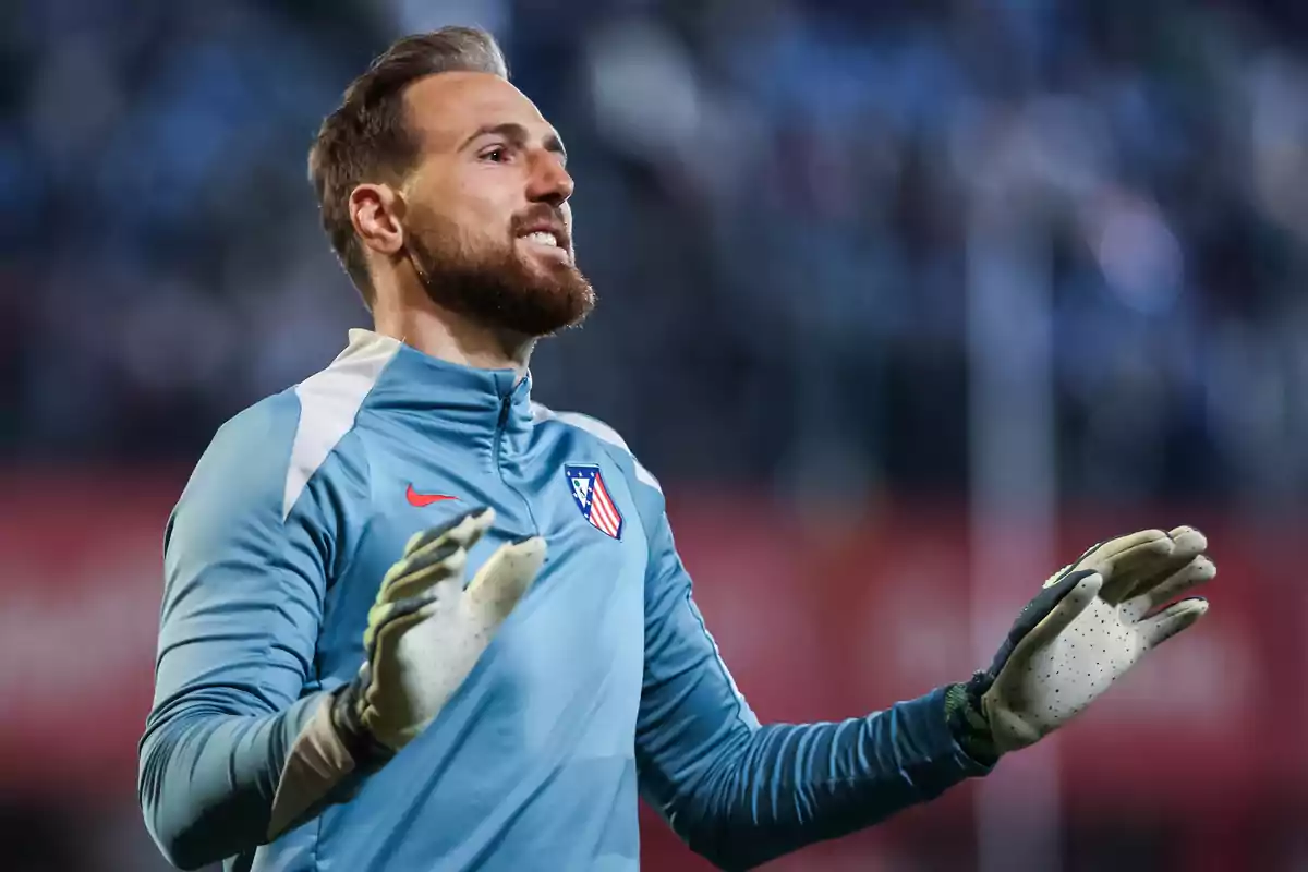 A soccer player in a goalkeeper uniform and gloves raises his hands in a stadium.