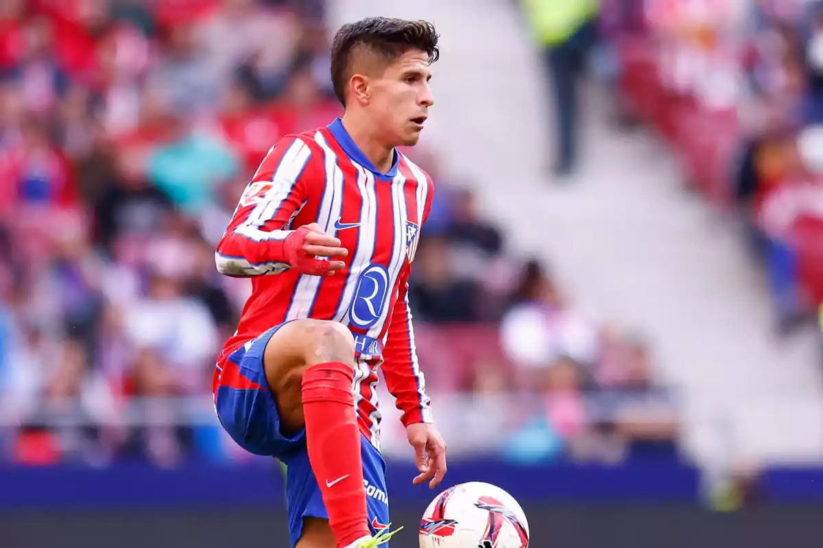 Jugador de fútbol con uniforme rojo y blanco controlando el balón en un estadio.